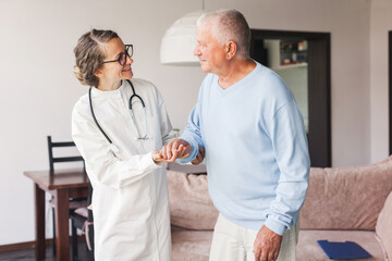 Female professional doctor showing medical test result explaining prescription using clipboard visiting senior elderly old man patient at home sitting on sofa