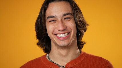 Portrait of smiling handsome gender fluid Latino Hispanic young man 20s wearing orange casual shirt...