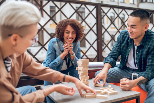 Joyous company employee observing her coworkers playing a board game
