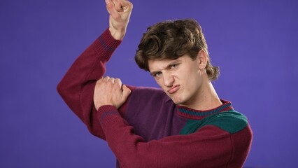 Portrait of young hipster man 20s with show muscles, have fun energy isolated on purple background in studio