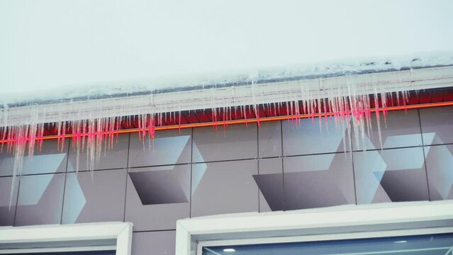 Large icicles hang from the overhang of the roof of the building. Falling ice- winter hazard for passersby