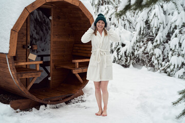 Portrait of caucasian woman standing in front of sauna wearing in bathrobe - obrazy, fototapety, plakaty
