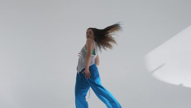 Modern dance, stylish young brunette in baggy blue pants dancing in jazz-funk style. Stylish and youthful. The dance hall is illuminated by sunlight, bright colors