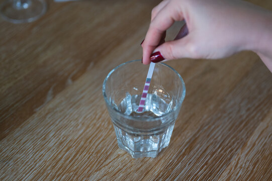 Woman's Hand Submerged In Glass Analysis Strip Test To Check Water Hardness At Home. Indicator Shows Very Hard Water.  Side View, Selective Focus.