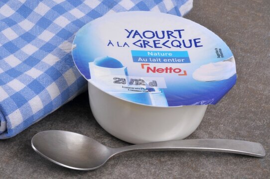 Yaourt à la grecque de la marque Netto avec une cuillère et une serviette de table en gros plan sur fond gris