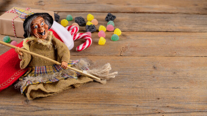 The funny witch Befana and red stocking with sweet coal and candy on rustic wooden background. Italian Epiphany day tradition, top view, flat lay, greeting card, web banner