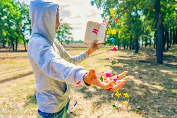 A man reads a book in the park, letters fly from above and fall on his hand, exhaustive knowledge in nature.