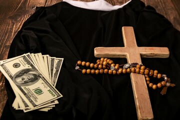 A Catholic cross, a rosary with beads and dollars lie on the black clothes of the priest before the...