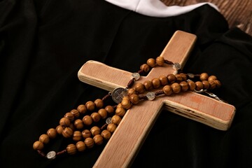 Catholic cross, rosary with beads lie on the black clothes of the priest.