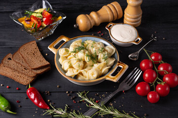 boiled dumplings with sour cream and gray bread, on a black background