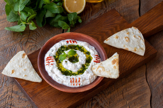 Turkish meze dish Haydari made from yogurt, cheese and fresh herbs. Dipping Sauce on a plate topped with a drizzle of olive oil and mint on top, with pita bread on the side for dipping. Horizontal