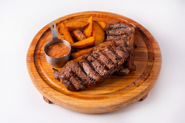 steak with potatoes and sauce on a round wooden board. on a white background