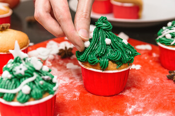 Baker making Christmas treat. Cupcakes shaped Christmas tree. Hands squeeze tasty cream from icing...