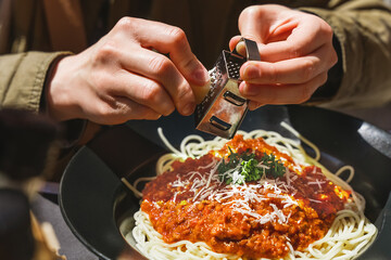 Hands grating delicious parmesan cheese on freshly made italian bolognese pasta. Small box of cheese grater. Italian cuisine, bolognese pasta recipe.