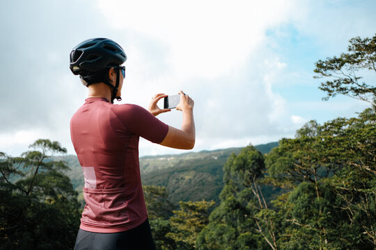 A young female cyclist is taking photos with her mobile device in the mountains.