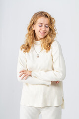 A young blonde girl with curly hair in a white knitted suit smiles and steps on a white background