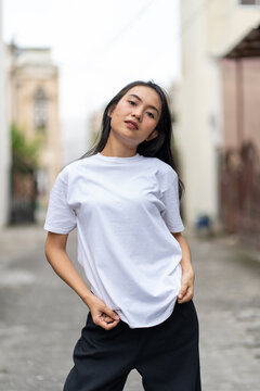 A young woman with a white blank shirt doing a cool pose with the with out of focus background