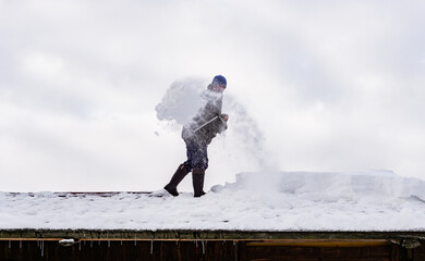Man in action cleaning snow from the private house roof with shovel . Danger 