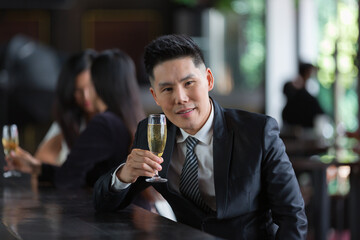 Asian businessman at bar counter with drinking beer, looking at camera and smiling