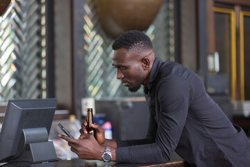 African American man at bar counter with drinking beer and using smart phone