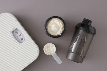 Gym diet nutrition concept. Flat lay photo made of whey protein in jar and shaker, scales on grey background with copy space. Minimal sport diet idea.