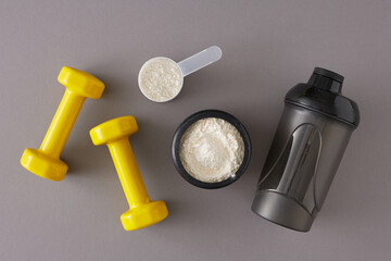 Gym diet nutrition concept. Top view composition made of protein powder in jar with shaker and dumbbells on grey background. Minimal sport diet idea. - obrazy, fototapety, plakaty