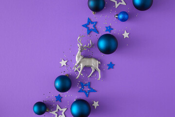 New Year card concept. Top view composition made of silver Christmas deer, baubles, sequins, stars on violet background with copy space. Minimal winter holiday postcard idea.