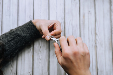 Obraz premium Hands of a woman, a girl close-up, making herself a manicure, cutting cuticles with special scissors on fingers, nails on a wooden white background. Close-up photography, work, beauty, art.