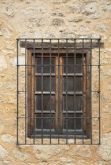 Fototapeta na wymiar Vintage casement window behind iron bars in limestone mud wall