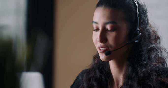 The call center operator communicates with the customer and consults about the products that her company offers. Asian female consultant with dark hair at work talking through a headset to a client