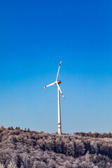 Wind turbine on the winter hill.  Wind farm against blue sky. Producing electric energy. Renewable energy. Vertical photo.