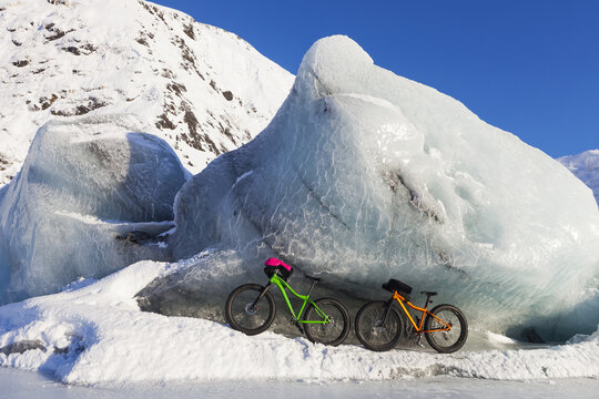 Fatbikes, 907 fat tire bike and Fatback fat tire bike, resting against giant iceberg in winter on Portage Lake, Chugach National Forest; Portage, Alaska, United States of America