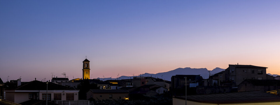 Skyline of the village of Benissanet at sunset with silhouetted mountains in the distance; Benissanet, Tarragona, Catalonia, Spain