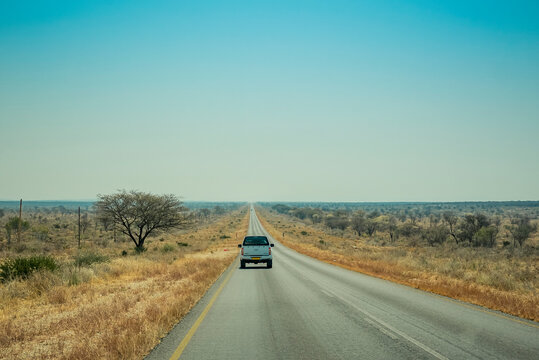 A Truck Drives On An Open Road In The Desert With A Big Blue Sky On The Horizon; Namibai