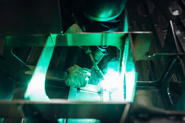 The worker makes spot welding of metal parts in the factory, sparks, and glow
