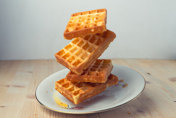 Flying waffles on a plate over a wooden table and white background