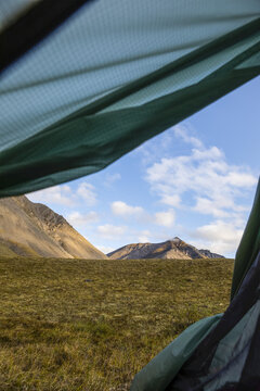 View outside door of green backpacking tent of mountains in the Brooks Range on a sunny day, Arctic National Wildlife Refuge; Alaska, United States of America