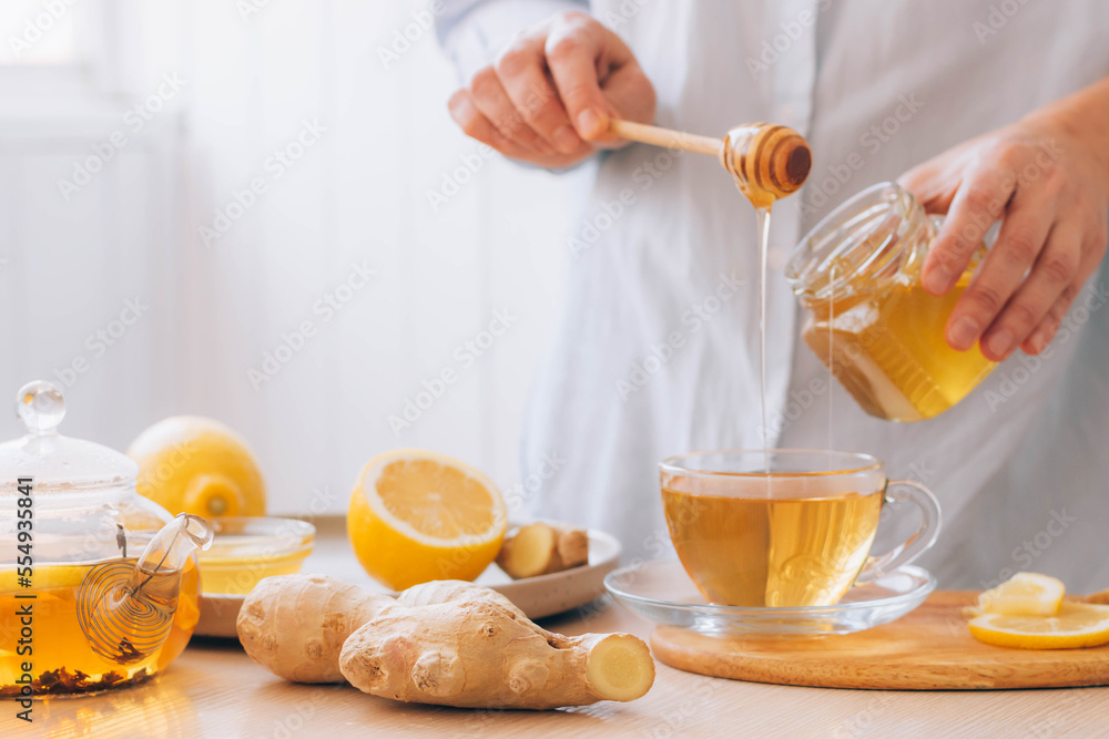 Wall mural women's hands prepare hot drink tea from ginger root lemon honey for cold treatment and prevention