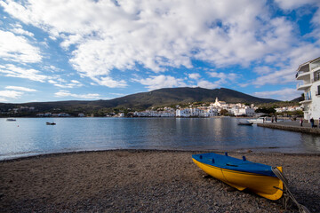 Fototapeta na wymiar Barca amarilla y azul estacionada en una de las playas de piedra del pequeño pueblo de cadaqués en un día de otoño.