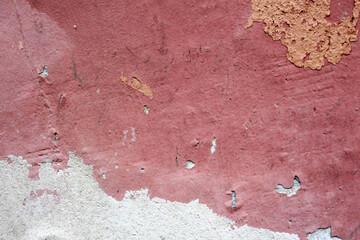 Pink rough painted wall of the house with pieces of fallen plaster pink city wallpaper