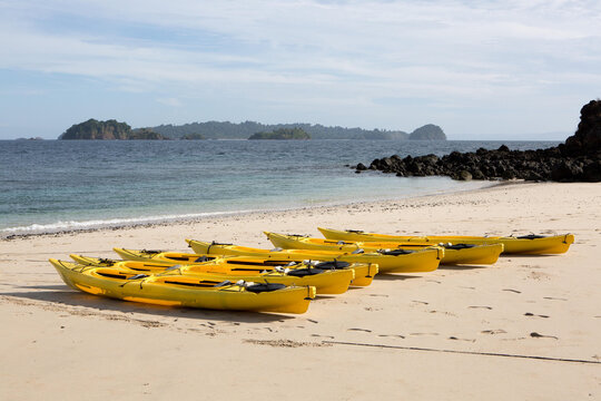 Yellow kayaks are neatly aligned on the sandy shore of the small island Isla Granito de Oro.; Isla Coiba National Park, Panama
