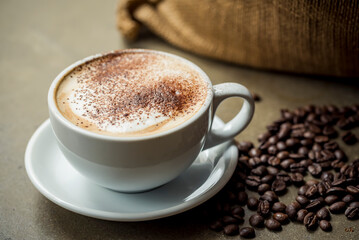 Cappuccino with foam and chocolate sprinkles and a sack and coffee beans on the counter beside the cup and saucer; Studio