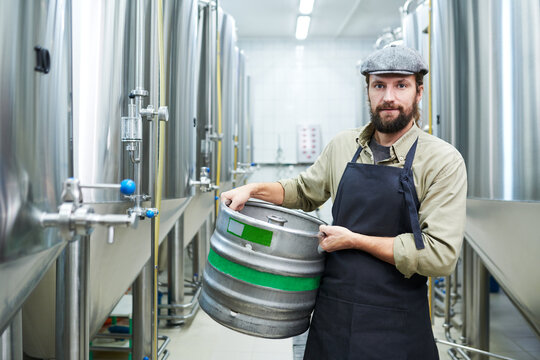 Portrait of beer manufacture worker holding keg and looking at camera