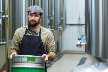 Bearded microbrewery owner carrying keg with beer to warehouse