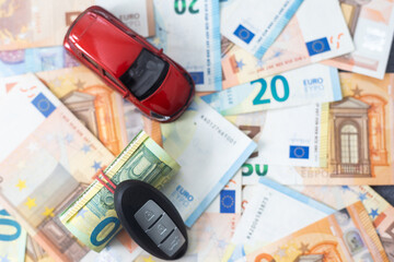 key and red toy car on pile of euro bills, buy or sell a car, rent a car or insurance concept.