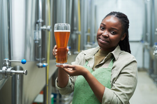Portrait of smiling small brewery worker showing glass of fresh beer