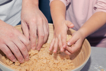 Obraz na płótnie Canvas girl's hands kneading cookie dough with her father in a bowl