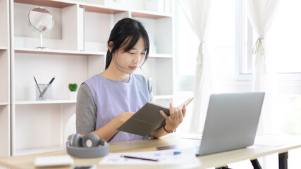 Fototapeta na wymiar Asian woman taking notes in notebook while studying online in laptop at home, Video chat, Online communication , Stay home, New normal, Distance learning.., Social distancing, Learn online...