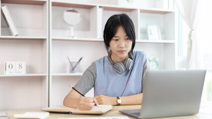 Asian woman taking notes in notebook while studying online in laptop at home, Video chat, Online communication , Stay home, New normal, Distance learning.., Social distancing, Learn online...