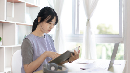 Young female student reading a book in a private office, Long distance education, Textbooks from books, Find out more, In the office there is a computer or laptop placed on the table, Study.